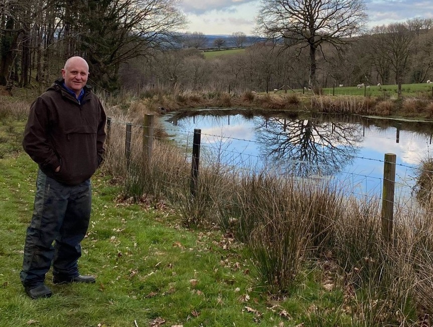 Hywel Morgan standing by a pond with trees behind him