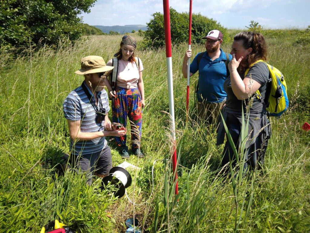 A group of people gather outdoors to talk about how to survey a sand dune.