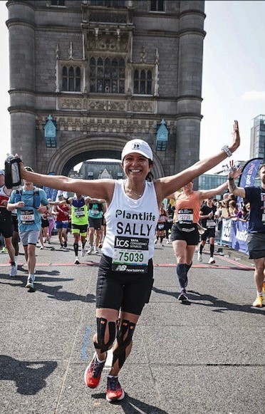 A woman running with her arms in the air and smiling, taking part in a race surrounded by other runners.