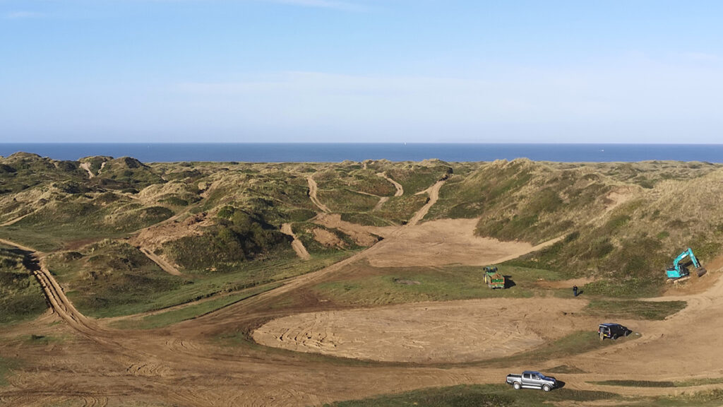 A landscape shot of a calm sea, blue sky and grassy dune areas with the diggers