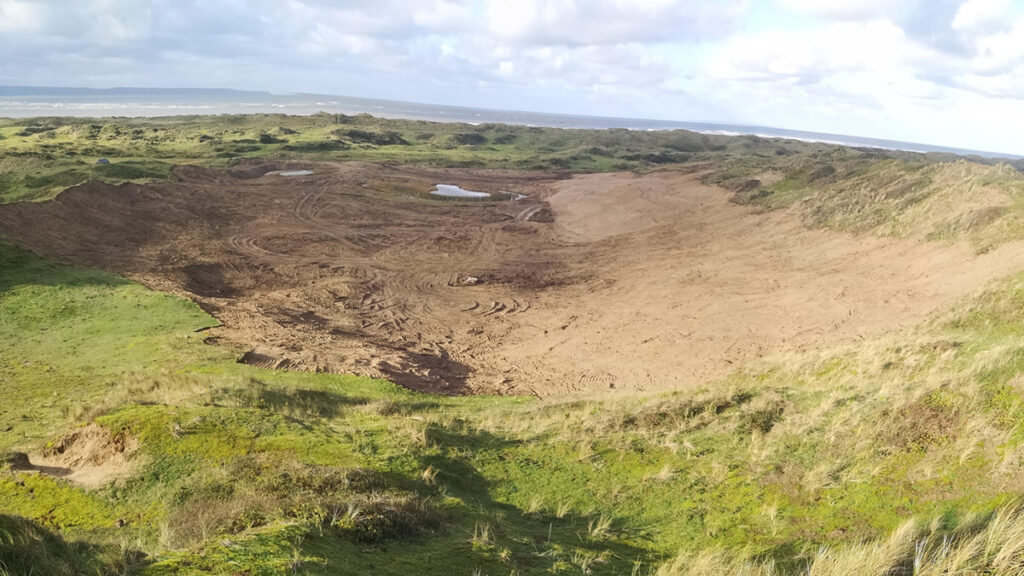 A landscape shot of a grassy dune scape with the sea in the distance