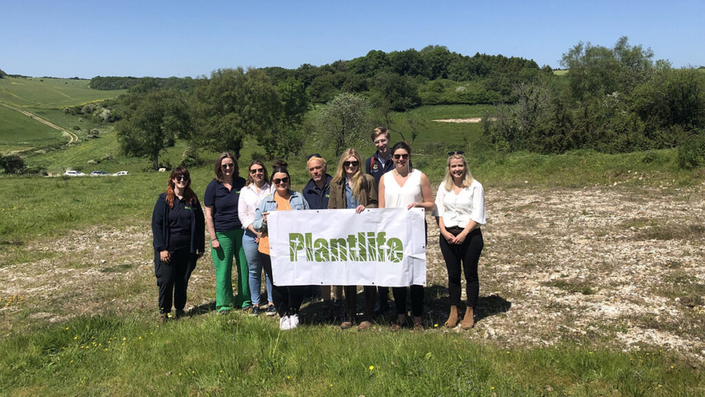 A group of people standing in a green field holding a white banner with the green Plantlife logo on it