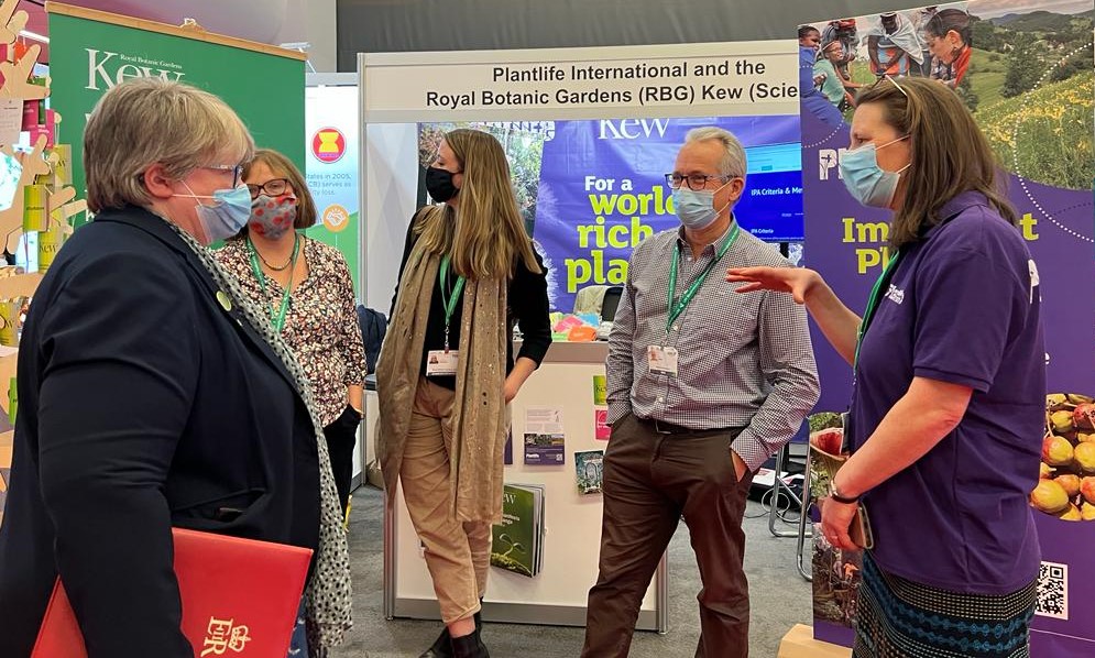 A group of people are stood next to a Plantlife event booth in a circle talking and listening to each other
