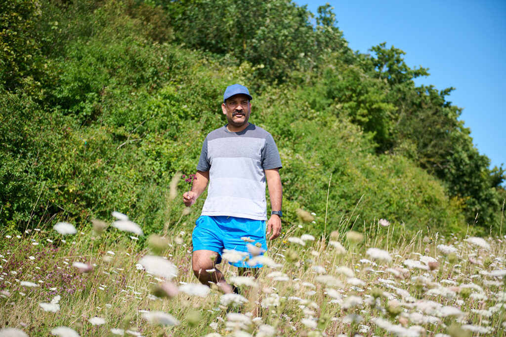 A man of colour wearing a blue hat and blue shorts walking through a wildflower field at Ranscombe Nature Reserve on a sunny day