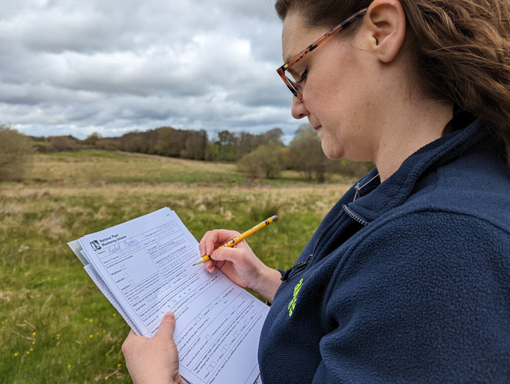 Rachel Murphy standing in a field filling in a paper form using a yellow pencil in her hands