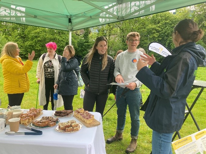 A group of people stood next to a table of refreshments listening to a Plantlife staff member talk