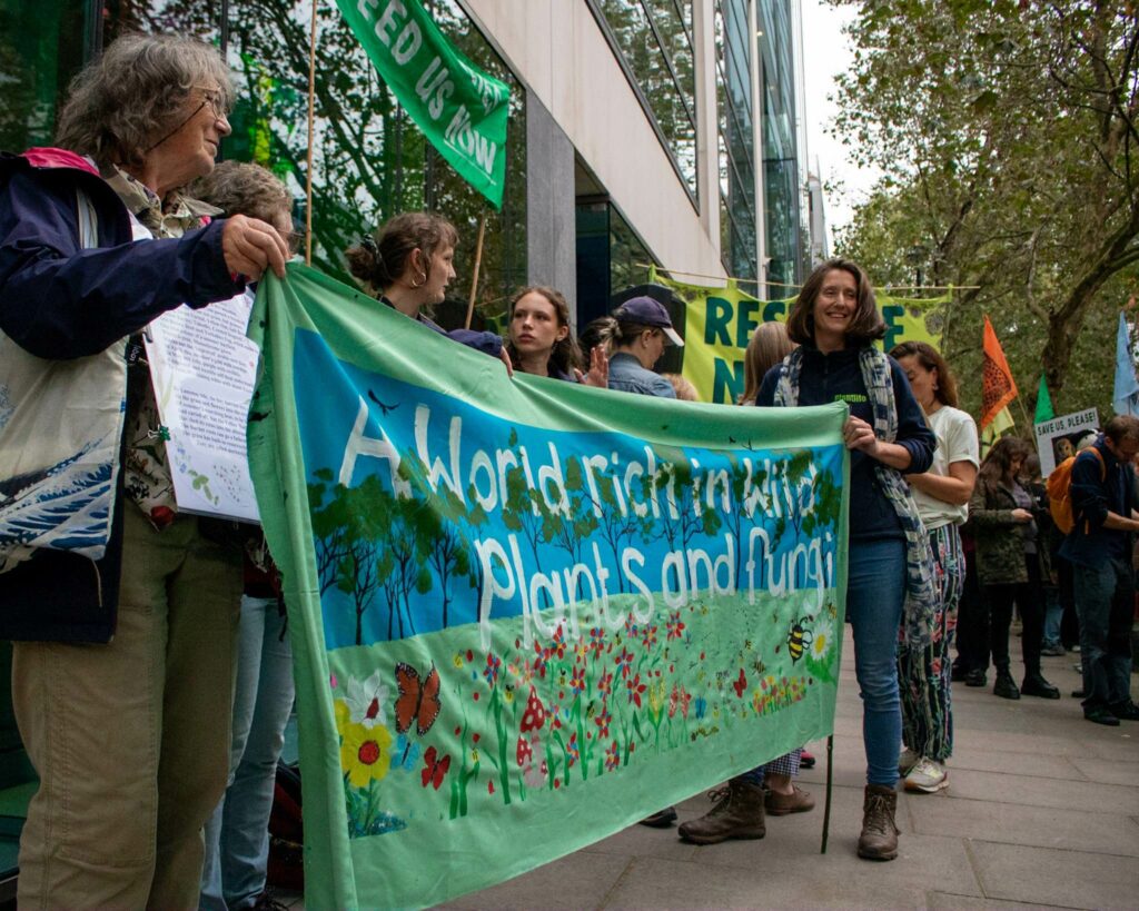 A group of protestors holding a banner which reads 'A world rich in plants and fungi'