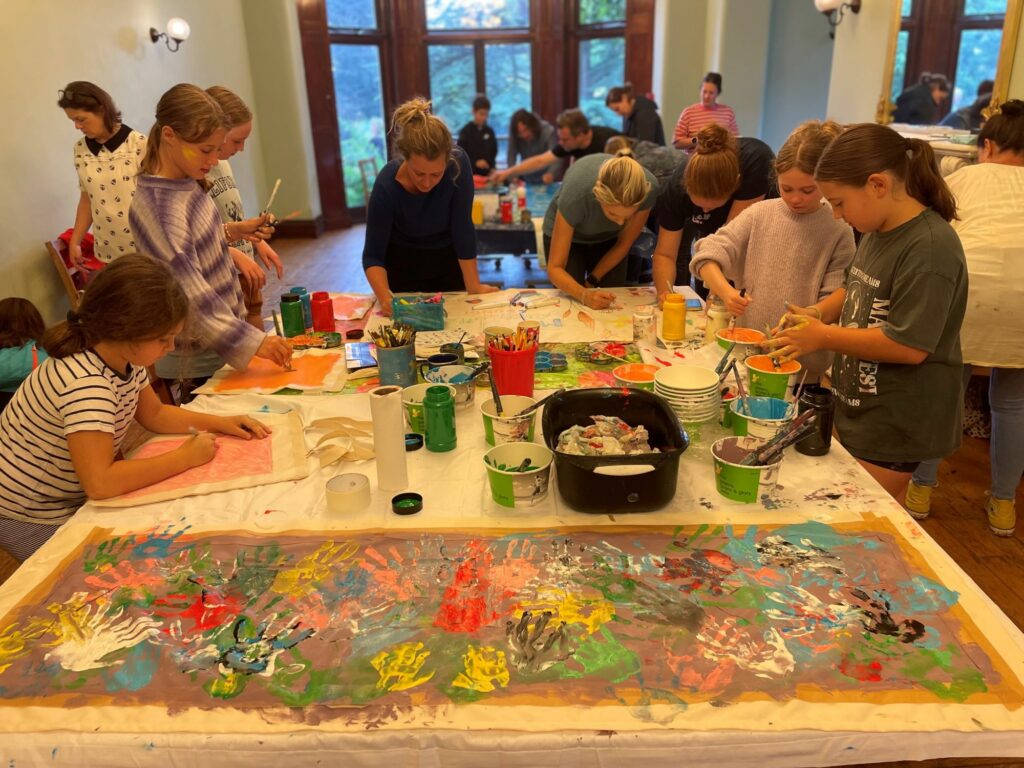 A group of children and adults painting banners in a room