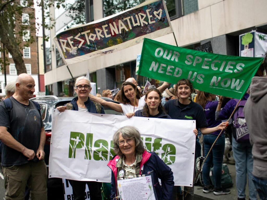A group of protestors with banners reading 'restore nature' and 'our species need us now'