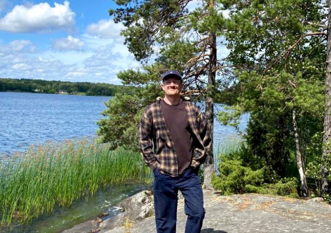A person standing in front of water and trees outside