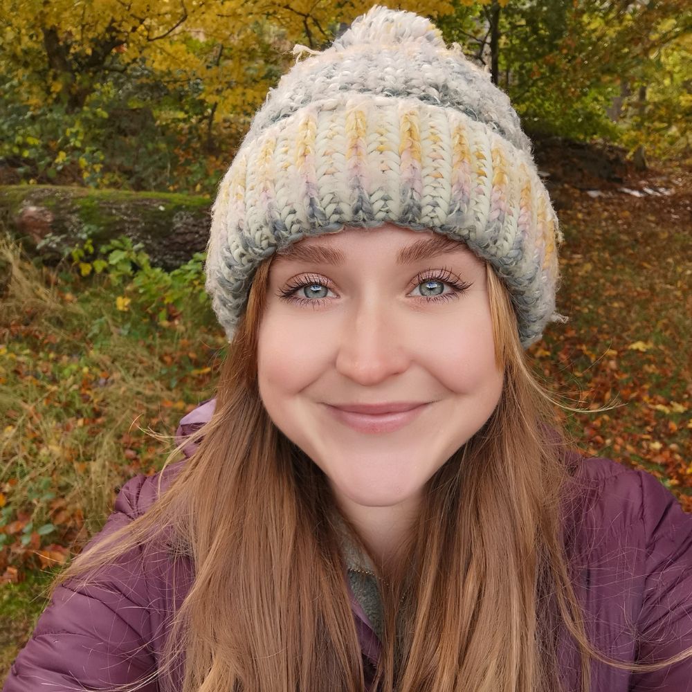 A person wears a woolly hat while standing in a forest