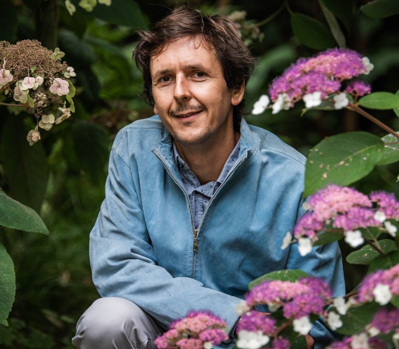 Image of Dan Bristow - Dan is positioned in the centre of the image. He is resting on one knee with his arm. Dan is surrounded by Hydrangea flowers