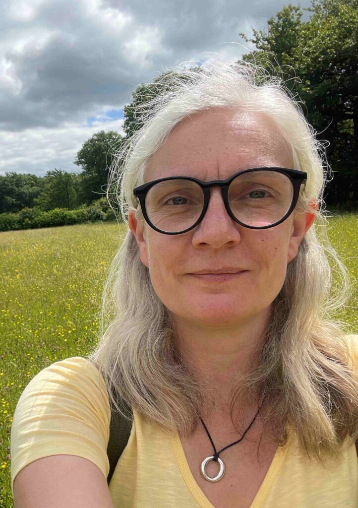 Our Deputy Chief Executive/Director of Conservation Nicola Hutchinson stands in a meadow on a sunny day. There are a few clouds in the sky and a boarder of trees on the horizon.