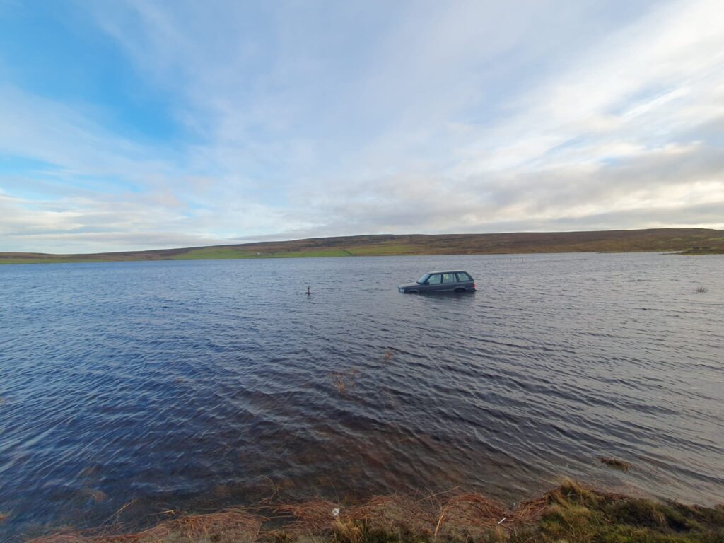 Image shows a large expanse of water. It could be mistaken for a large lake - however the water is actually covering a car park at a nature reserve in Scotland. A car is visible in the middle of the water and it can be seen to be over the wheel arches.