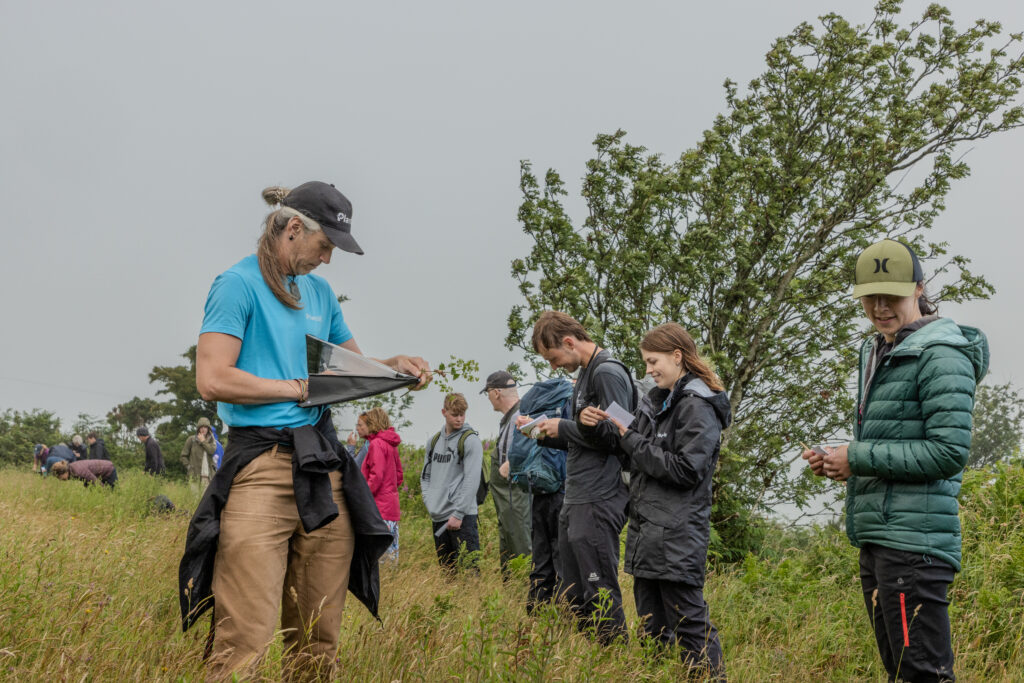 A group of people stand in a meadow, they have notepads and pens in hand and are helping take part in a survey