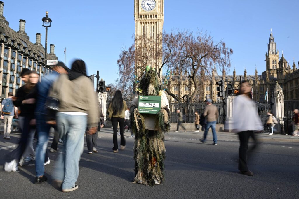 Someone wearing a bog costume holding a box showing 16,000 have signed a petition in front of Parliament