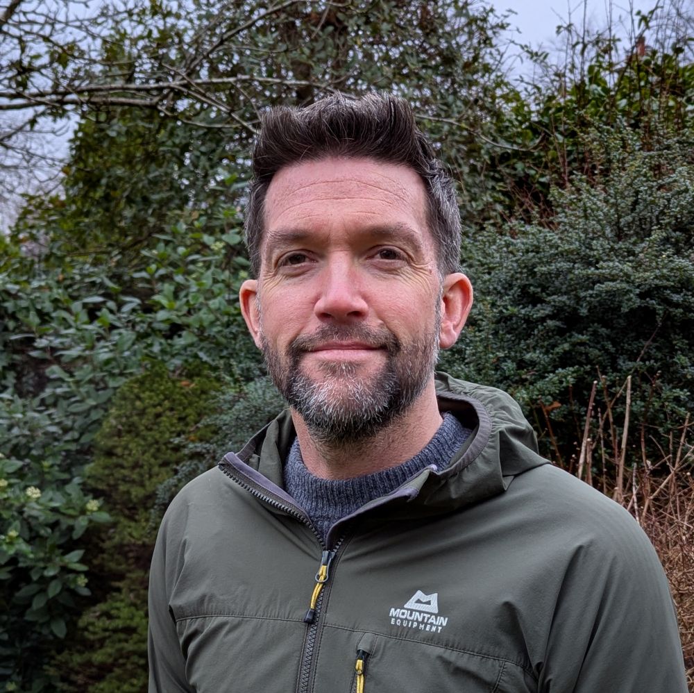 Photograph is a headshot of Alistair Whyte. He has dark hair and a beard. He is wearing a green hoody.