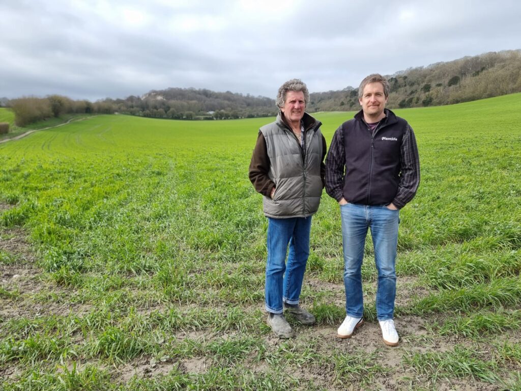 Two men stood together in front of a field on a farm