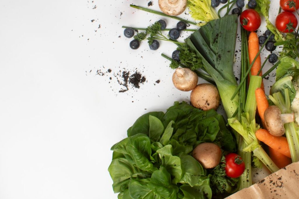 Photograph shows vegetables spilling out on to a white table from a brown paper bag. Over the vegetables and on to the white surface are bits of peat - showing that peat was used in the growing process for all of these every day vegetables.